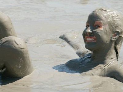 Person lying in a mud bath with mud covering her face and hair