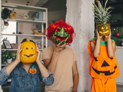 family holds up pumpkin, watermelon and pineapple as edible green Halloween costumes