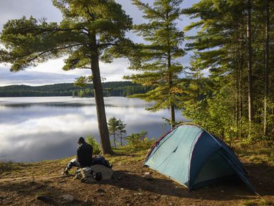 Man sitting on a rock next to a tent with a view of Provoking Lake in Algonquin Provincial Park