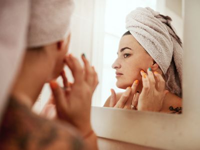 Woman treating blackhead and clogged pores in mirror.