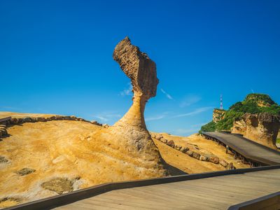 Queen's Head at Yehliu Geopark with a bright blue sky behind the carving and a wooden boardwalk below