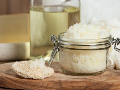 Handmade lemon sugar scrub in a glass jar with oil behind it.