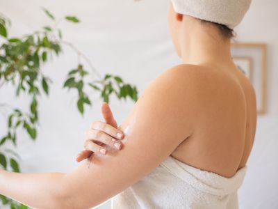 woman wrapped in white towel after shower applies lotion humectant